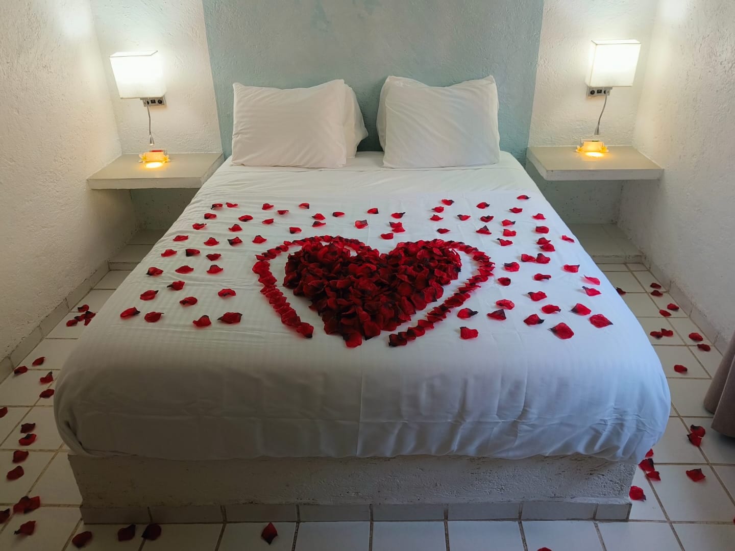 Cama de un bungalow de Portal Azahualco con un corazón de pétalos de rosa y las lámparas encendidas