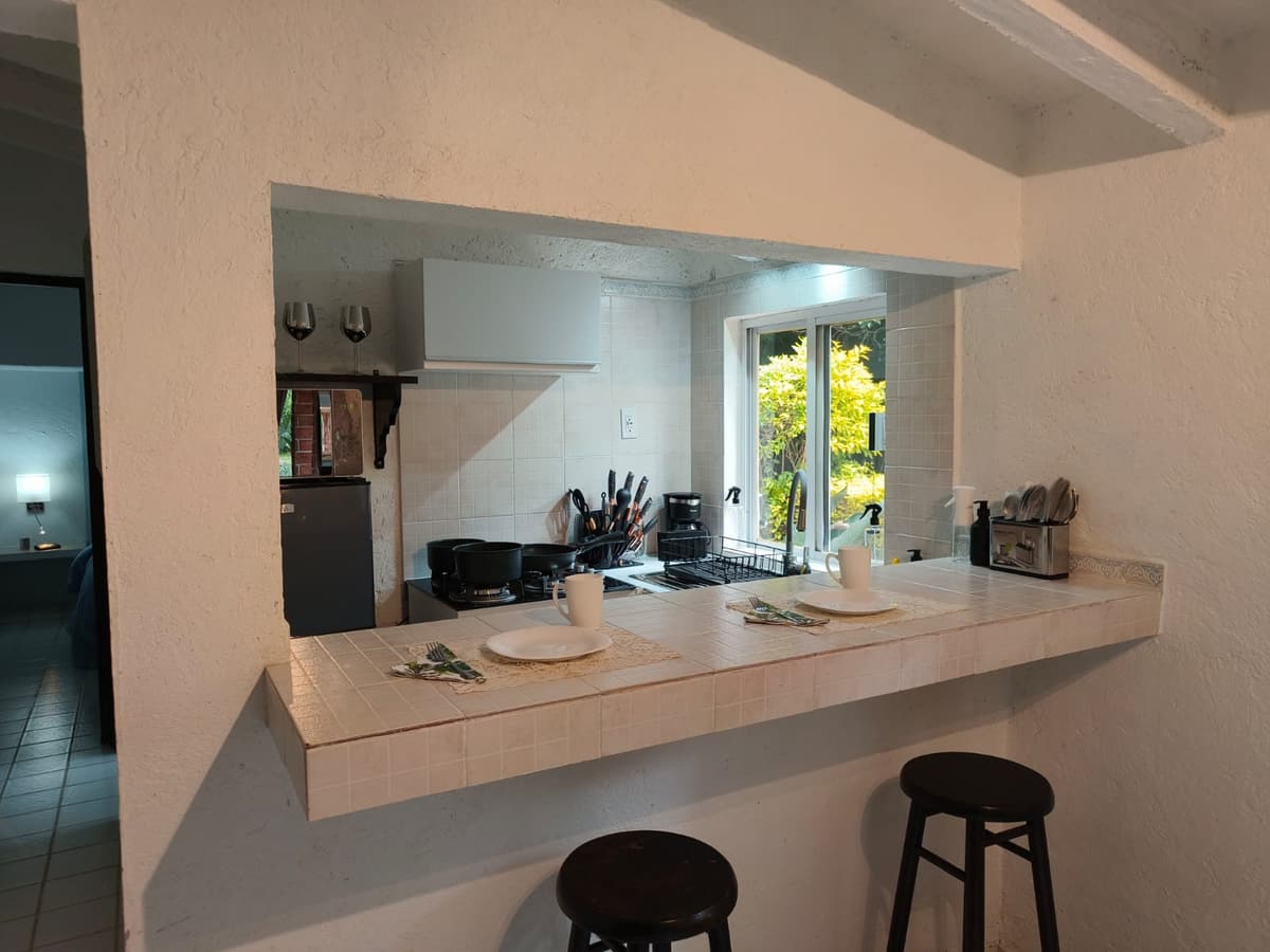 Cocina del Bungalow 1 vista desde la barra, con estufa, cafetera, sartenes y ventana al jardín