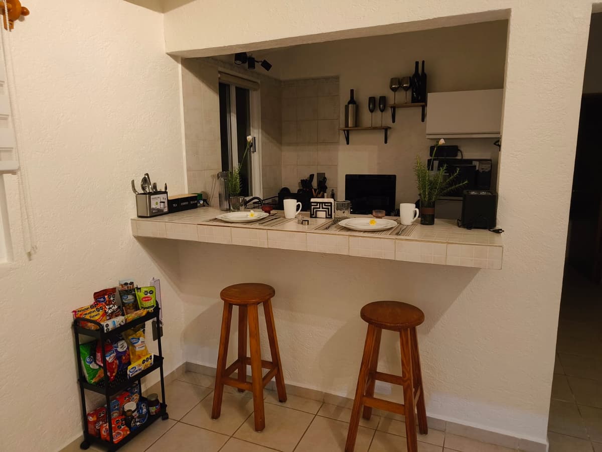 Barra de la cocina del Bungalow 2 con bancos de madera, mesa puesta para dos y el carrito del mini súper con botanas